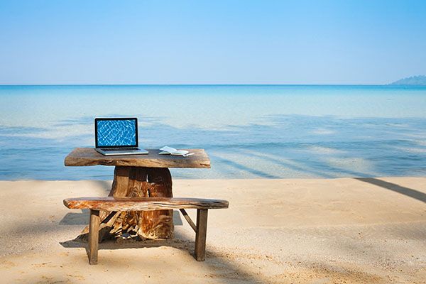 Image d'ordinateur seul sur la plage évoquant le besoin d'un soutien psy pour digital nomads et influenceurs